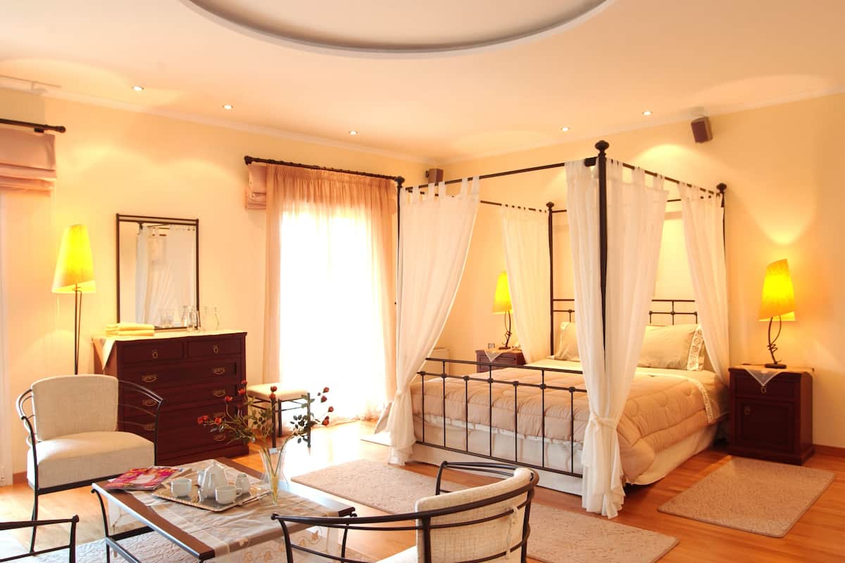 A bedroom with a four-poster bed, bedside lamps, a dresser, a chair, and a small table with a vase of flowers.