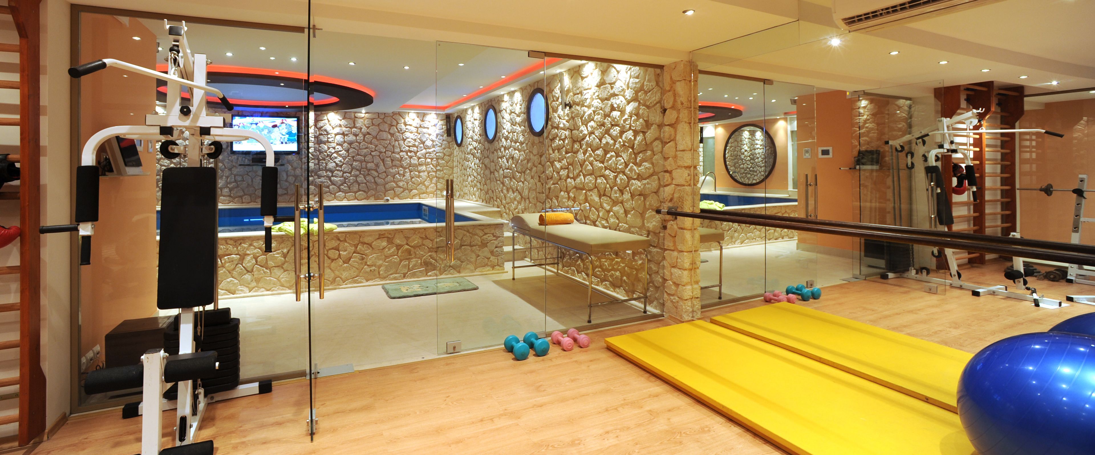 A gym with exercise equipment, a yellow mat, and a stone wall.