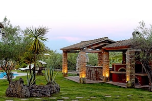 Un’area patio con barbecue in mattoni e posti a sedere, immersa nel verde e con una piscina.