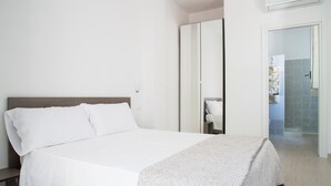 Habitación de hotel con cama, armario y baño visible a través de una puerta abierta.