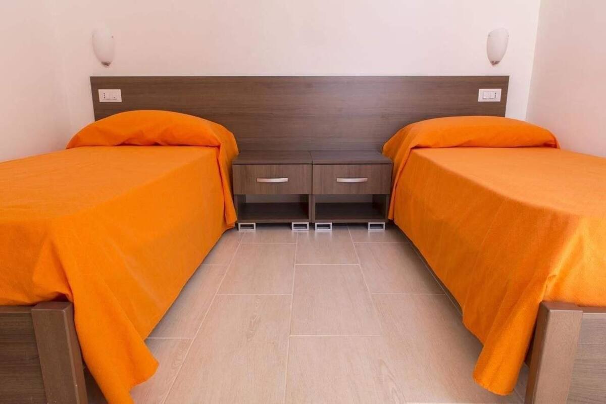 A twin room with two beds, each with an orange bedspread, a wooden headboard, and a small bedside table with drawers.