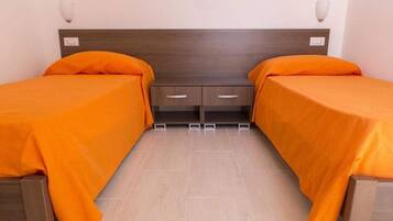 Habitación doble con dos camas, cada una con colcha naranja, cabecero de madera y mesita de noche con cajones.