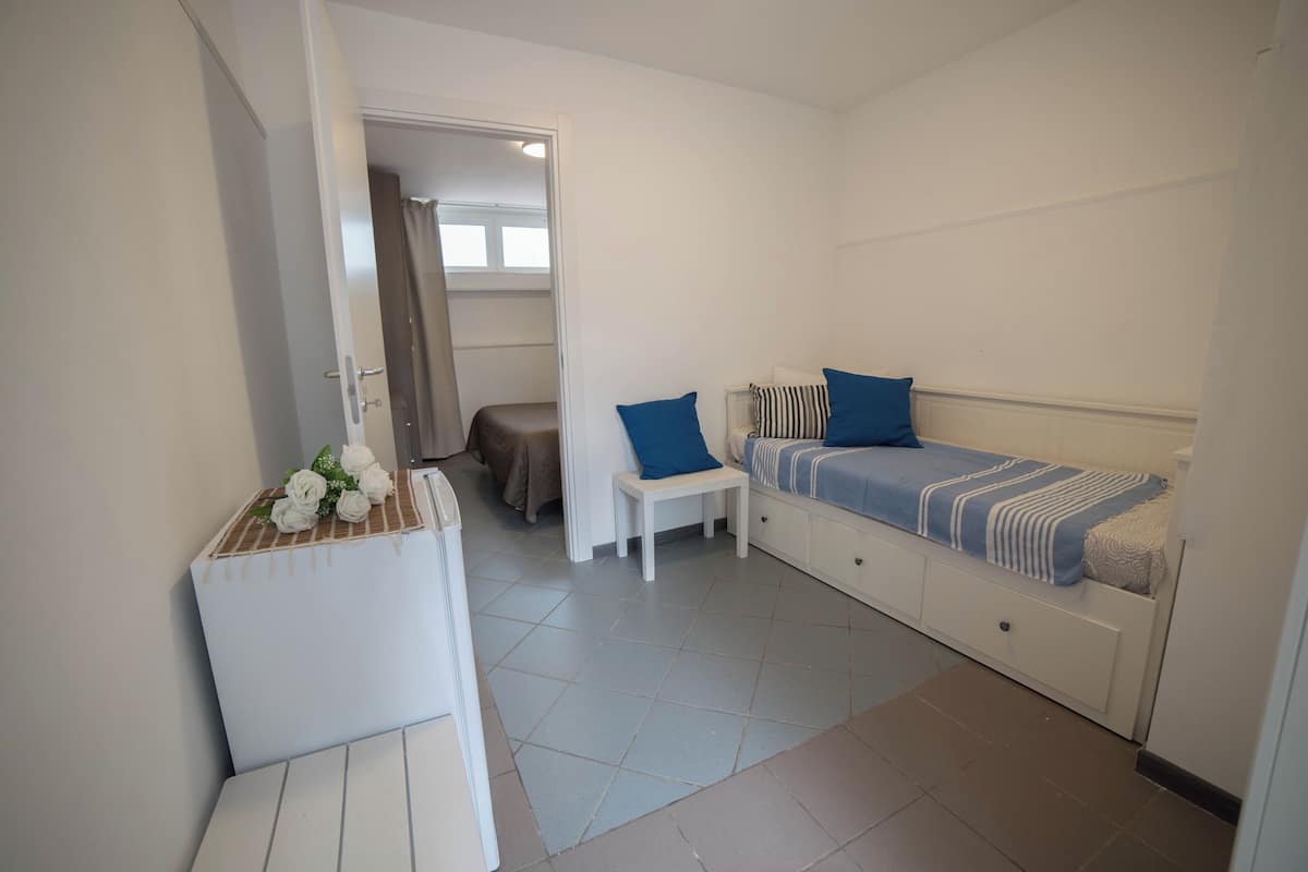 A compact room with a bed, a small table with flowers, a bench, and a door leading to another room.