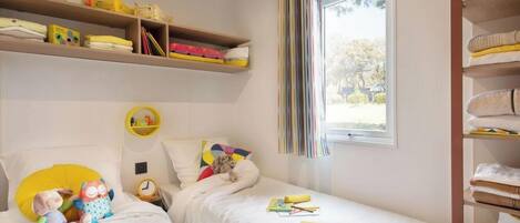 Quarto de criança com duas camas, uma estante de brinquedos e uma janela com cortinas.
