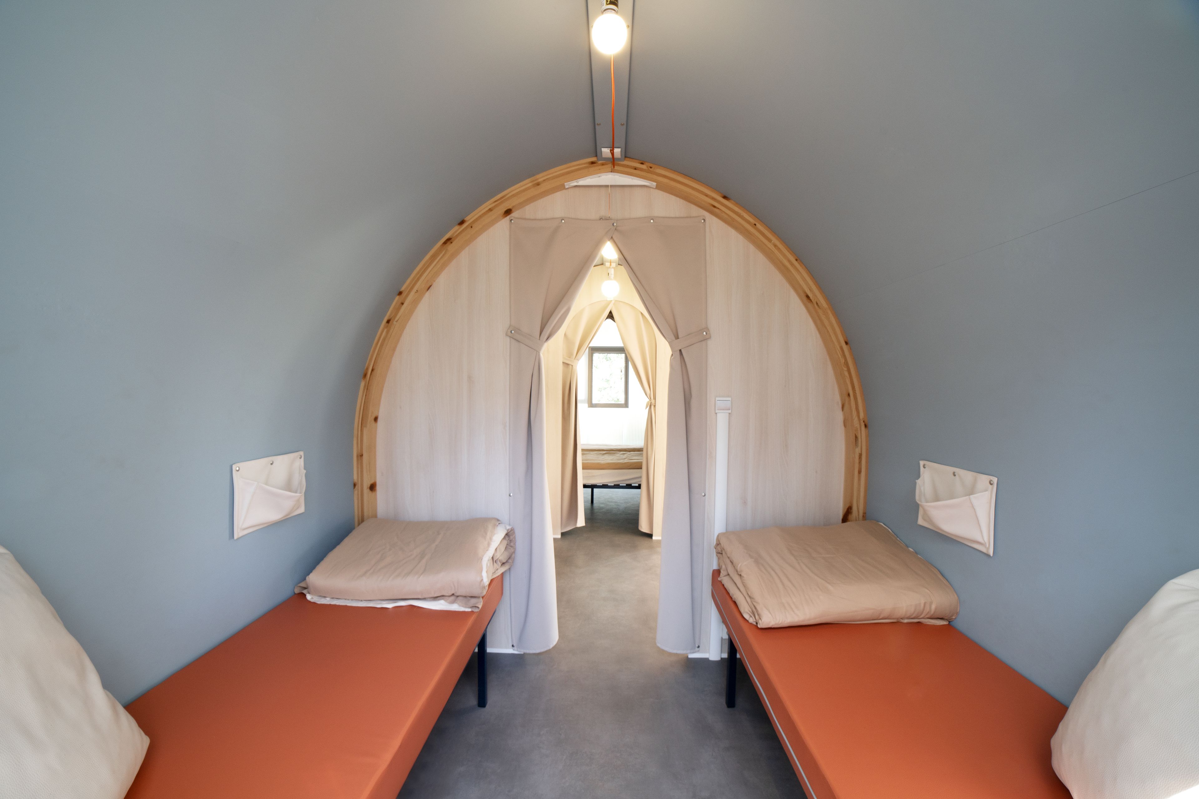 Quarto pequeno com duas camas, teto em arco de madeira e luminária.