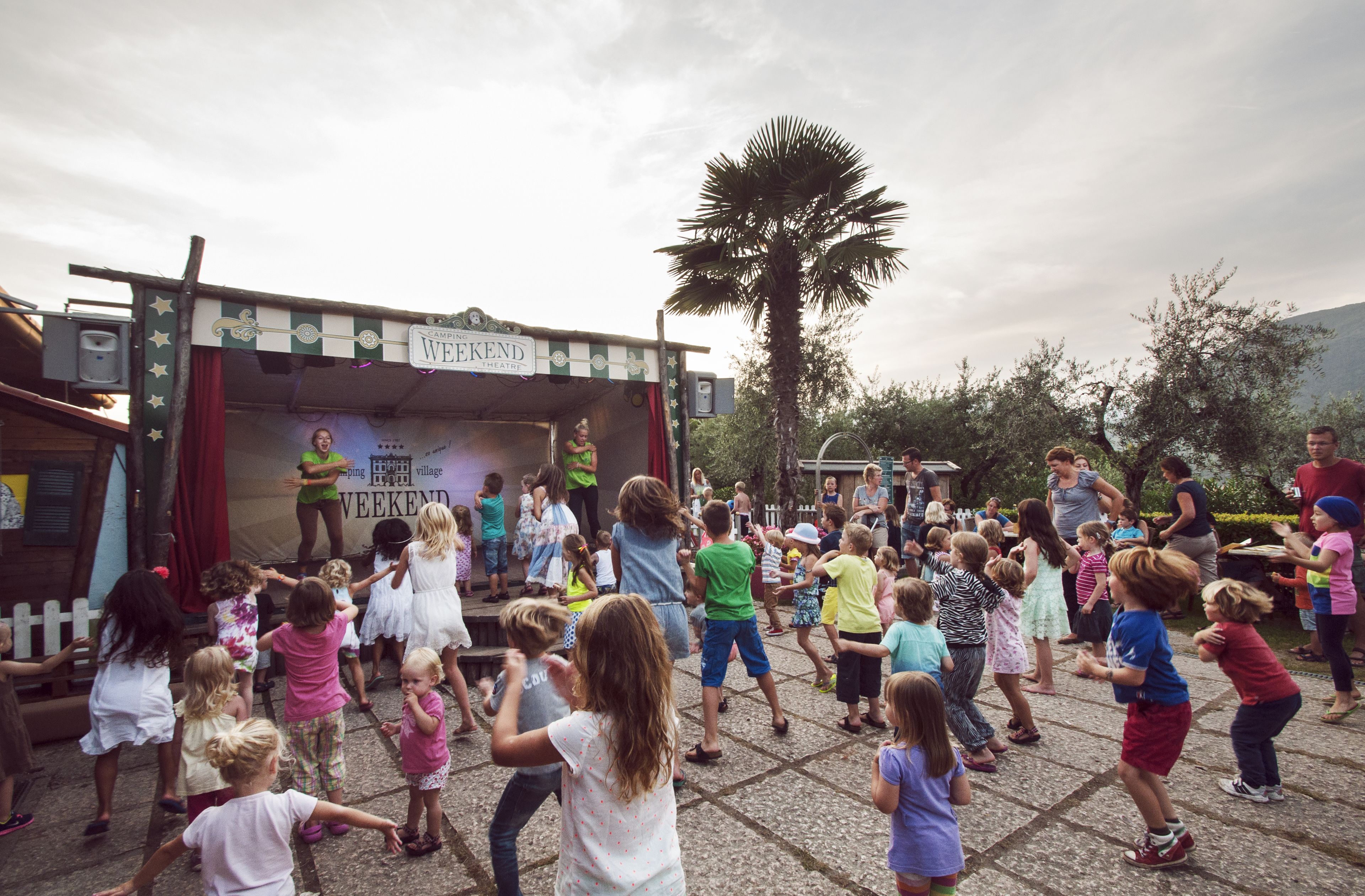 A group of children dancing on a stage with a sign that reads "WECKEND".