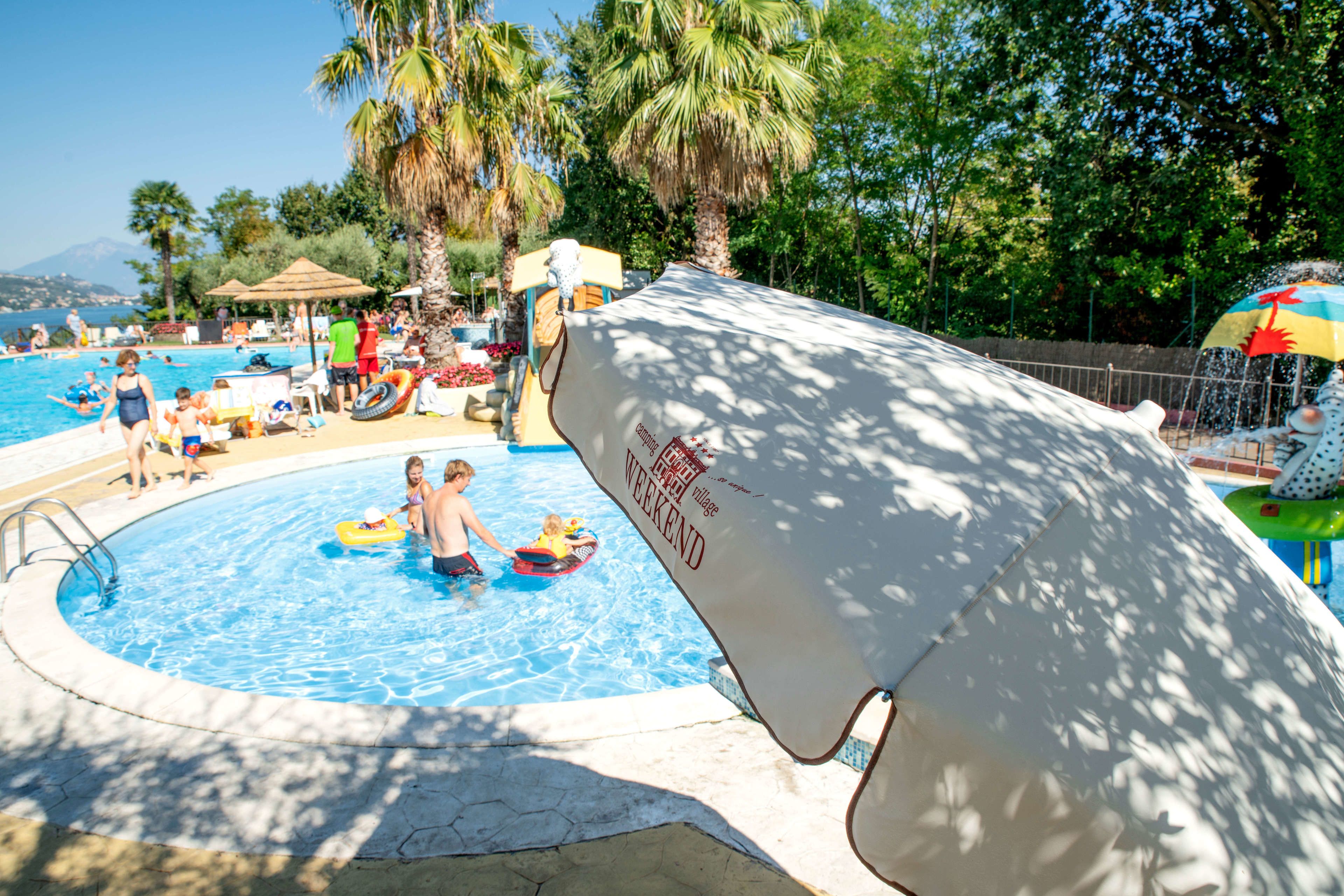 Una piscina con gente, palmeras y una zona cubierta.