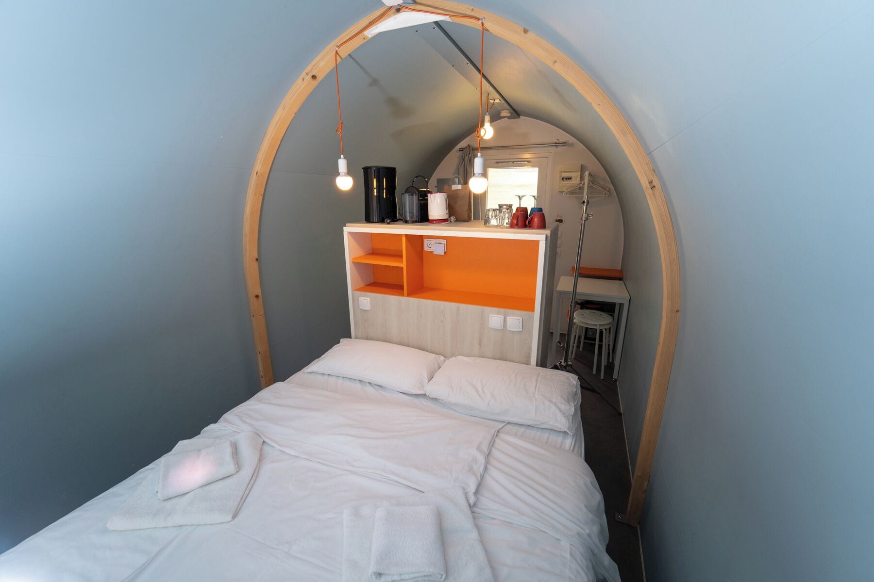 Una habitación pequeña con cama, una mesita y una kitchenette.