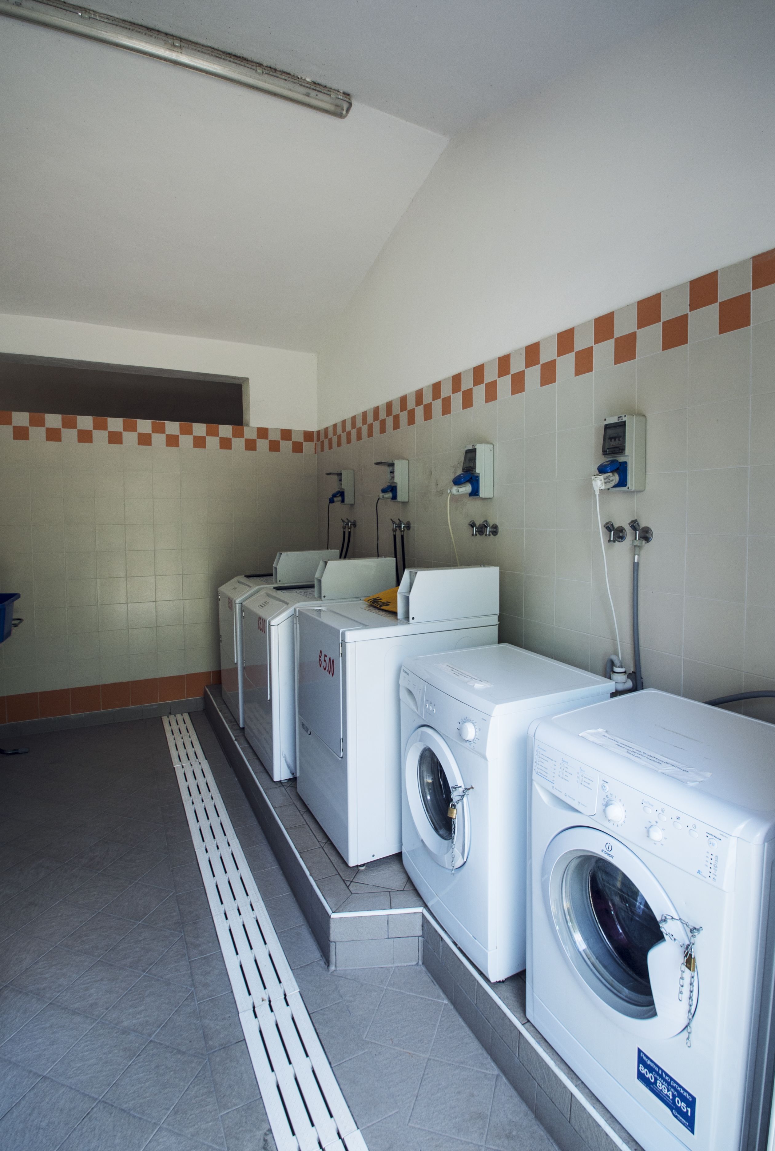 Une buanderie équipée de trois machines à laver et de trois sèche-linge superposés, d’un sol carrelé et d’un chauffe-eau fixé au mur.
