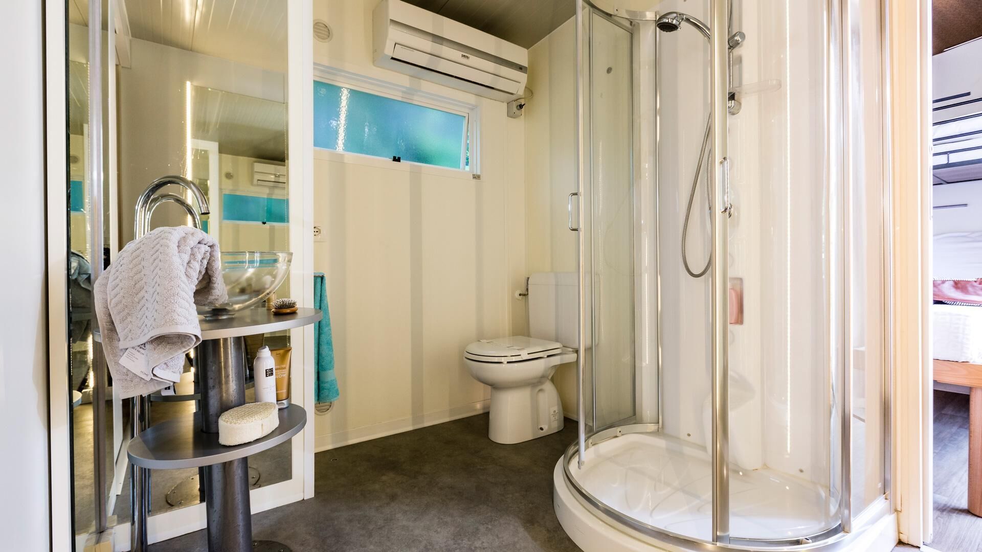 A bathroom with a glass-enclosed shower, a toilet, and a vanity with a towel rack and toiletries.