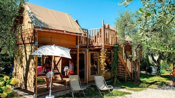 A wooden cabin with a covered porch, outdoor seating, and a staircase leading to an upper deck.