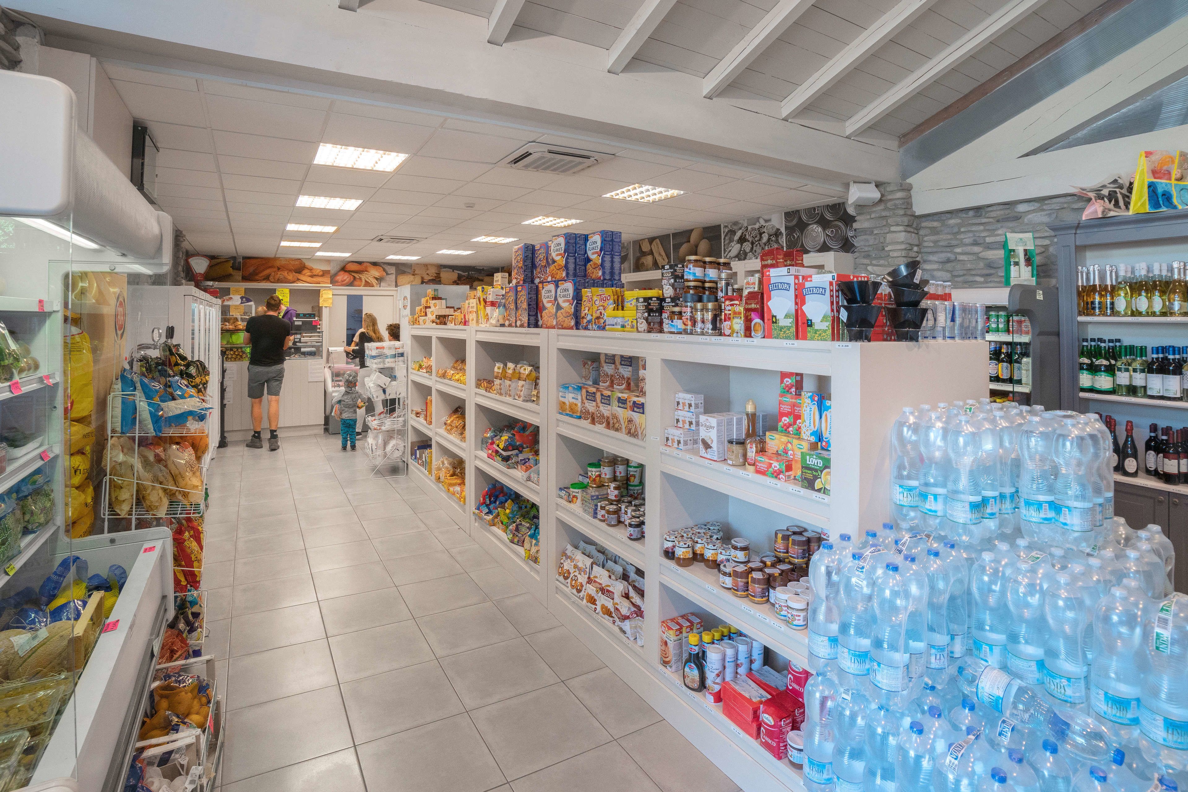 Un pasillo de supermercado con estantes llenos de diversos productos alimenticios y un congelador a la izquierda.