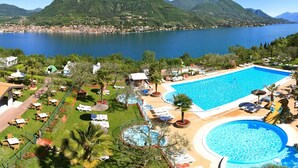 Un resort con una amplia piscina, una piscina circular más pequeña y un jardín bien cuidado con sillones y sombrillas.
