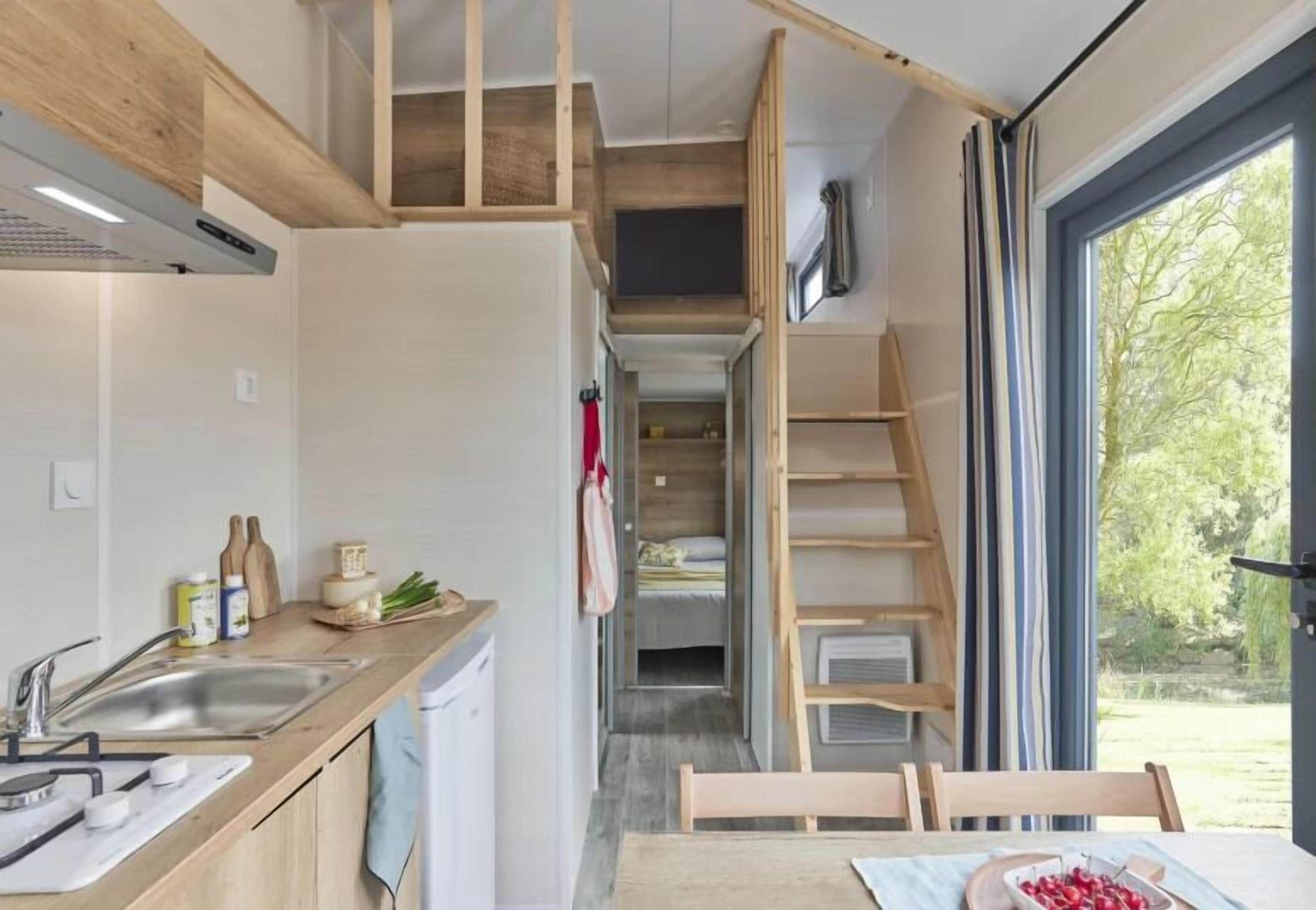 A compact kitchen with a sink, wooden counter, and a dining area with a table and chairs. A lofted sleeping area is visible above the kitchen.