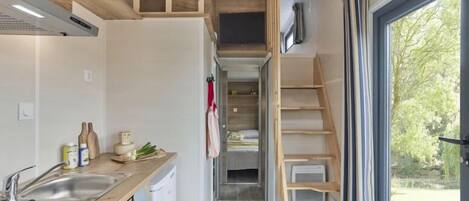 A compact kitchen with a sink, wooden counter, and a dining area with a table and chairs. A lofted sleeping area is visible above the kitchen.