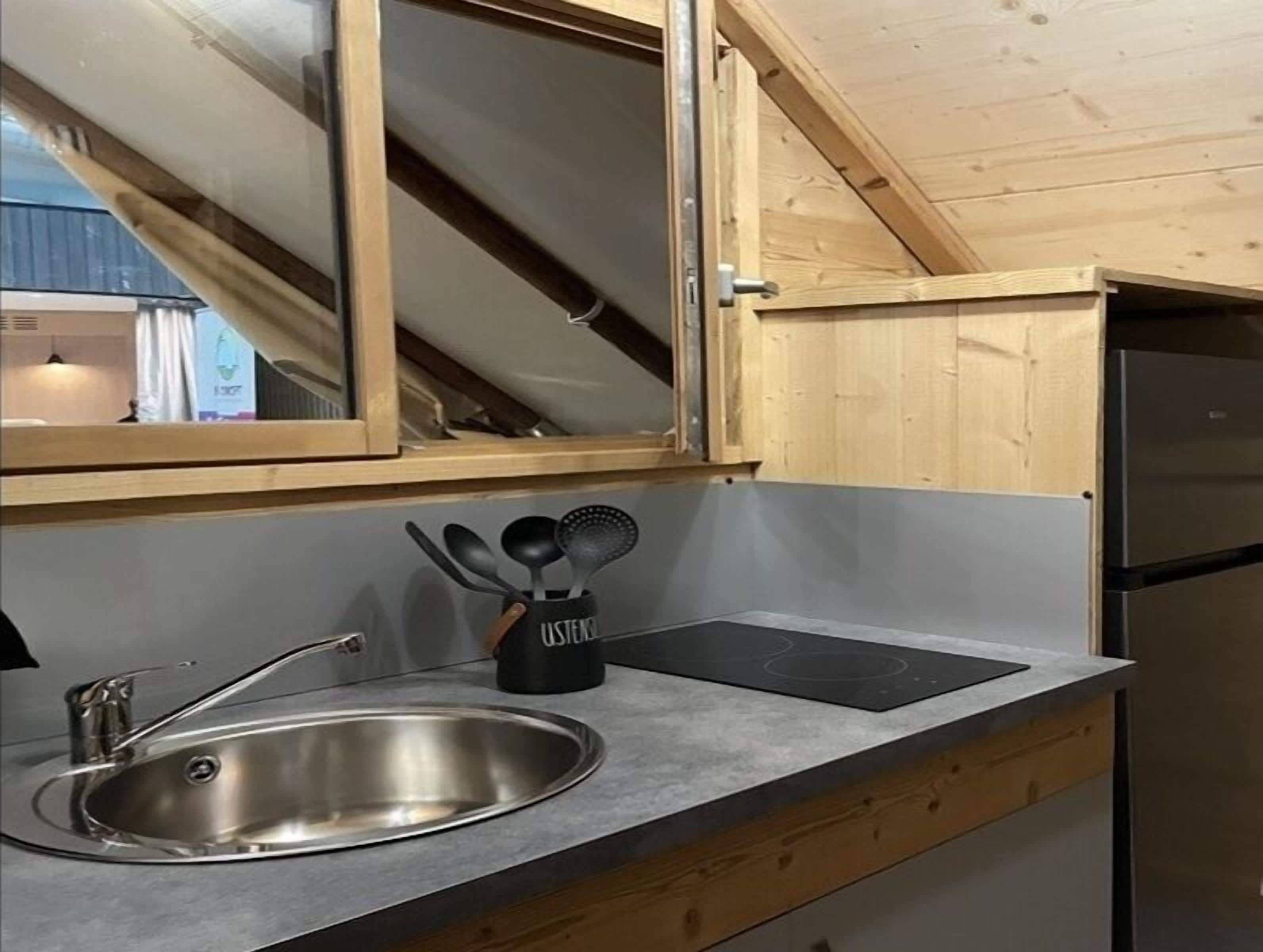 Een moderne keuken met een spoelbak van roestvrij staal, houten kastjes, een zwarte keukengerei houder en een ingebouwd fornuis.