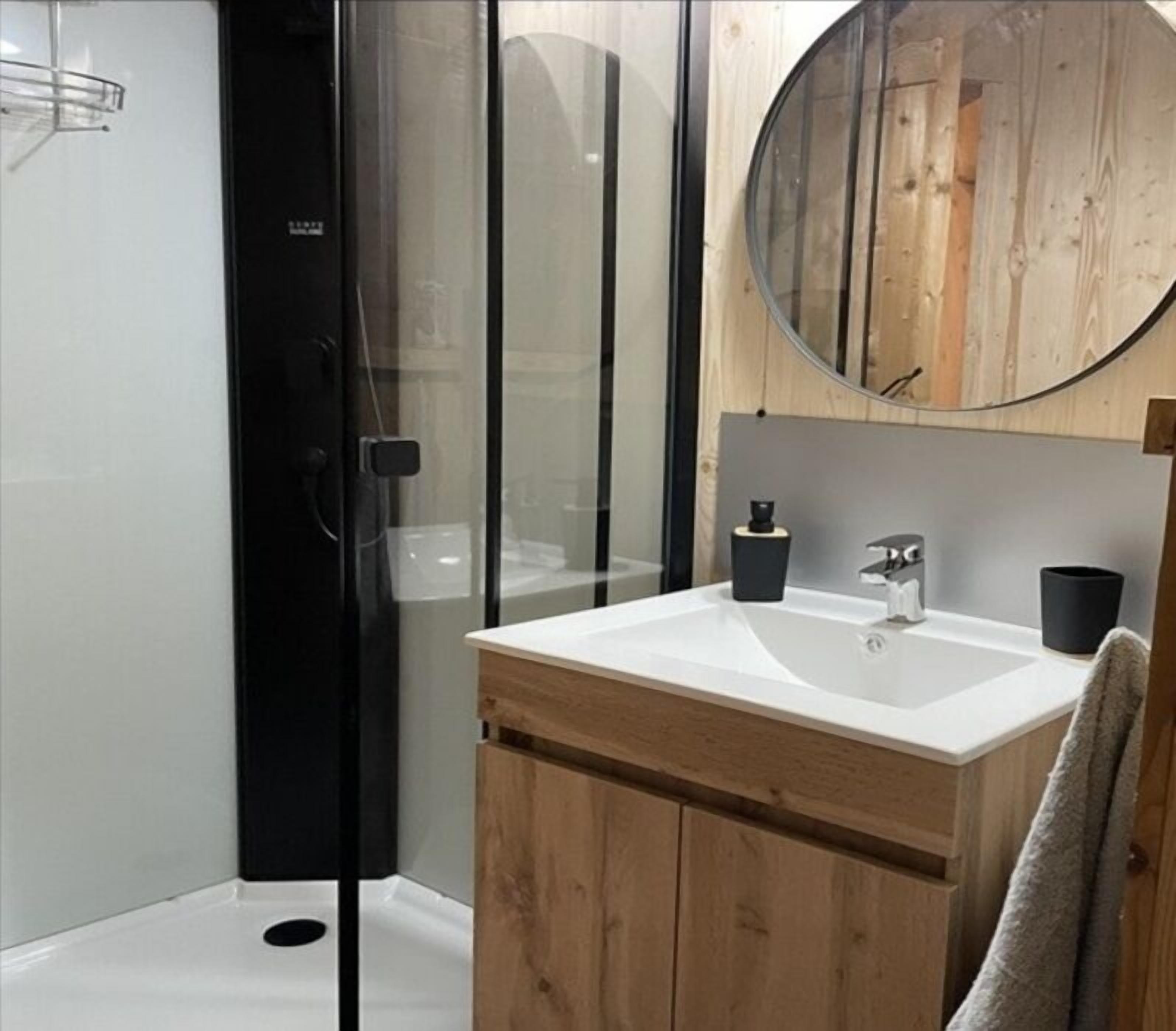 A modern bathroom with a glass shower enclosure, a wooden vanity with a sink, and a round mirror.