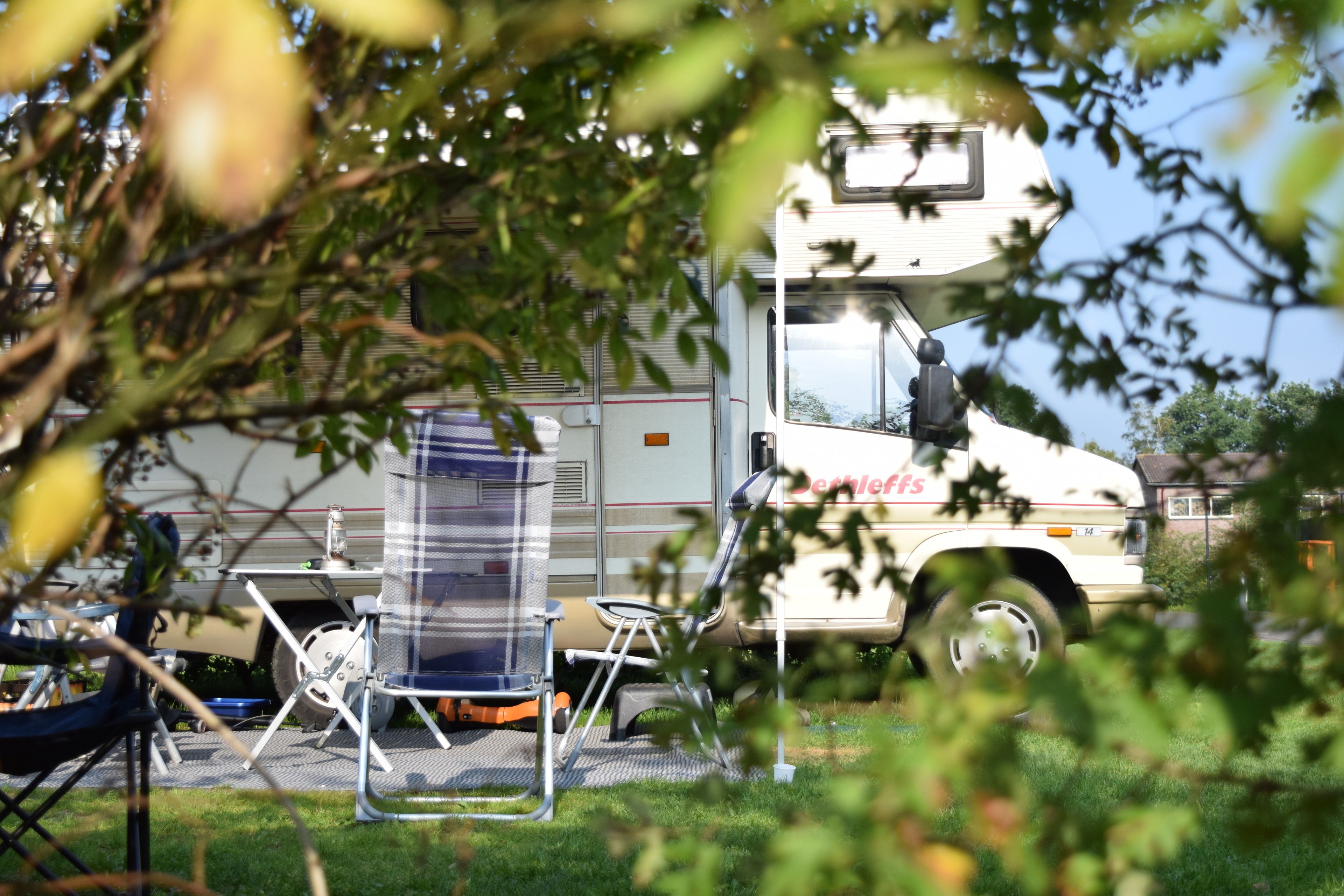 Een witte vrachtwagen met 'Beverly Hills' op de zijkant, geparkeerd in een grasveld met tuinmeubilair en een heldere lucht op de achtergrond.