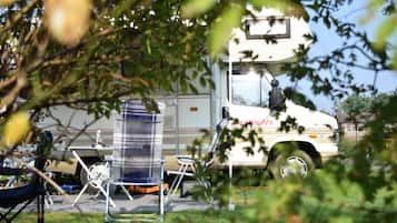 Een witte vrachtwagen met 'Beverly Hills' op de zijkant, geparkeerd in een grasveld met tuinmeubilair en een heldere lucht op de achtergrond.