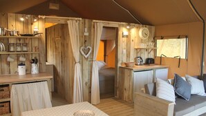 Un alojamiento en tienda de campaña acogedor, con interior de madera, comedor, kitchenette y zona de estar con cojines.
