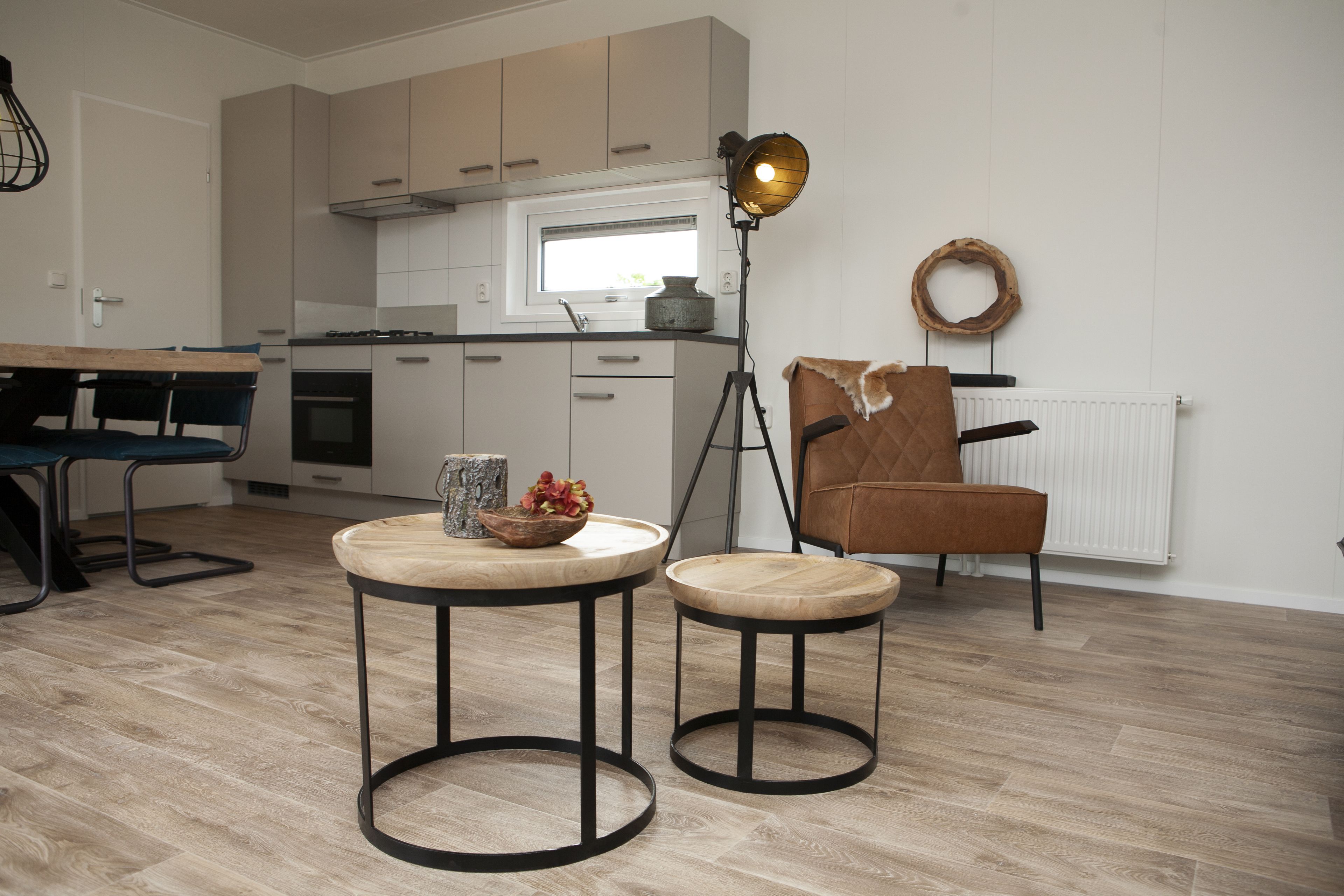 A modern kitchen with a dining area, including a table with stools, a pendant light, and a chair with a leather seat.