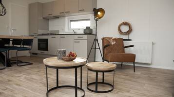 A modern kitchen with a dining area, including a table with stools, a pendant light, and a chair with a leather seat.