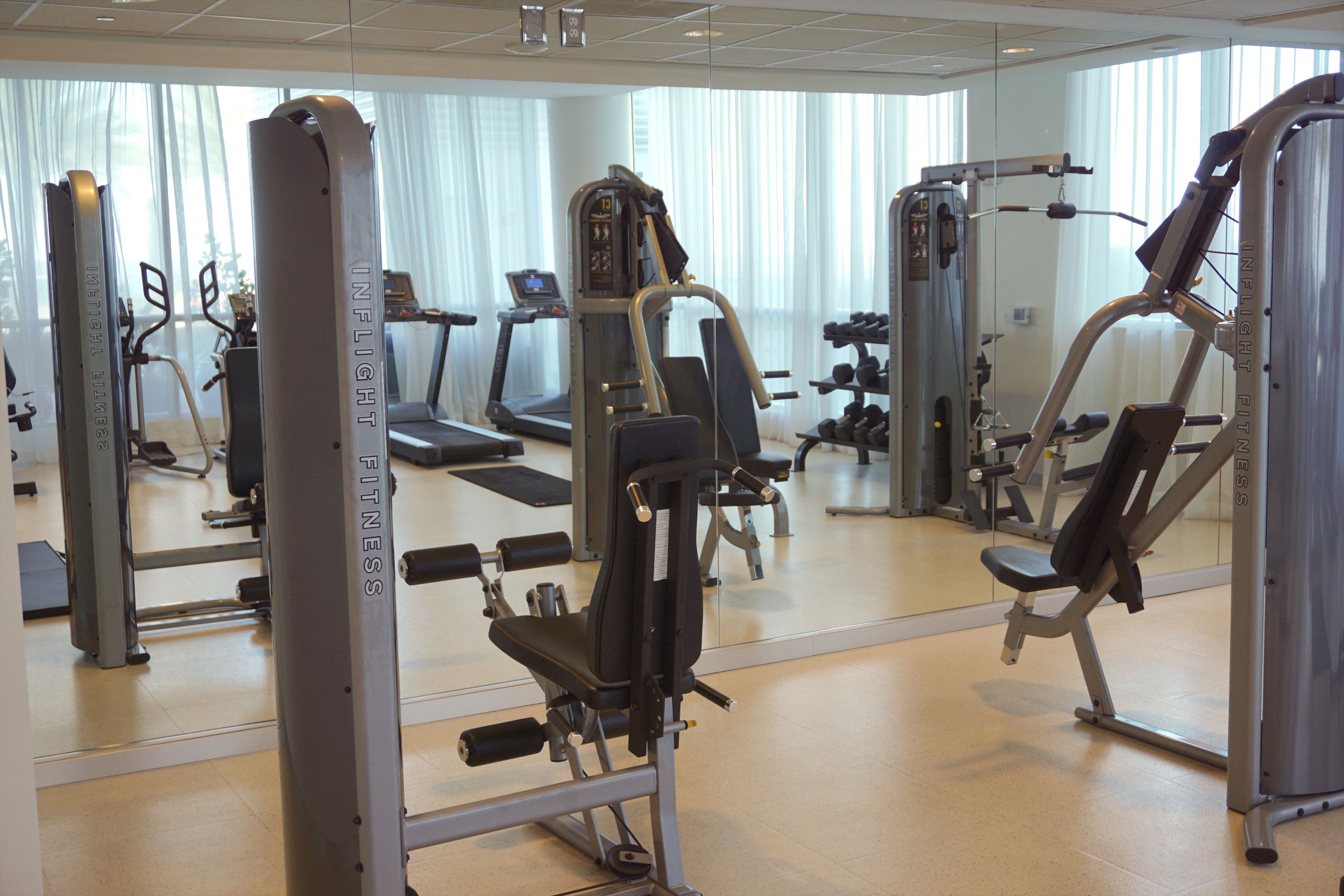 A gym with various exercise machines, a treadmill, and a mirrored wall.