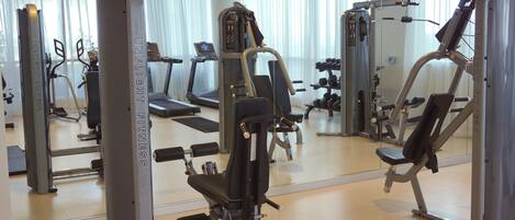 A gym with various exercise machines, a treadmill, and a mirrored wall.