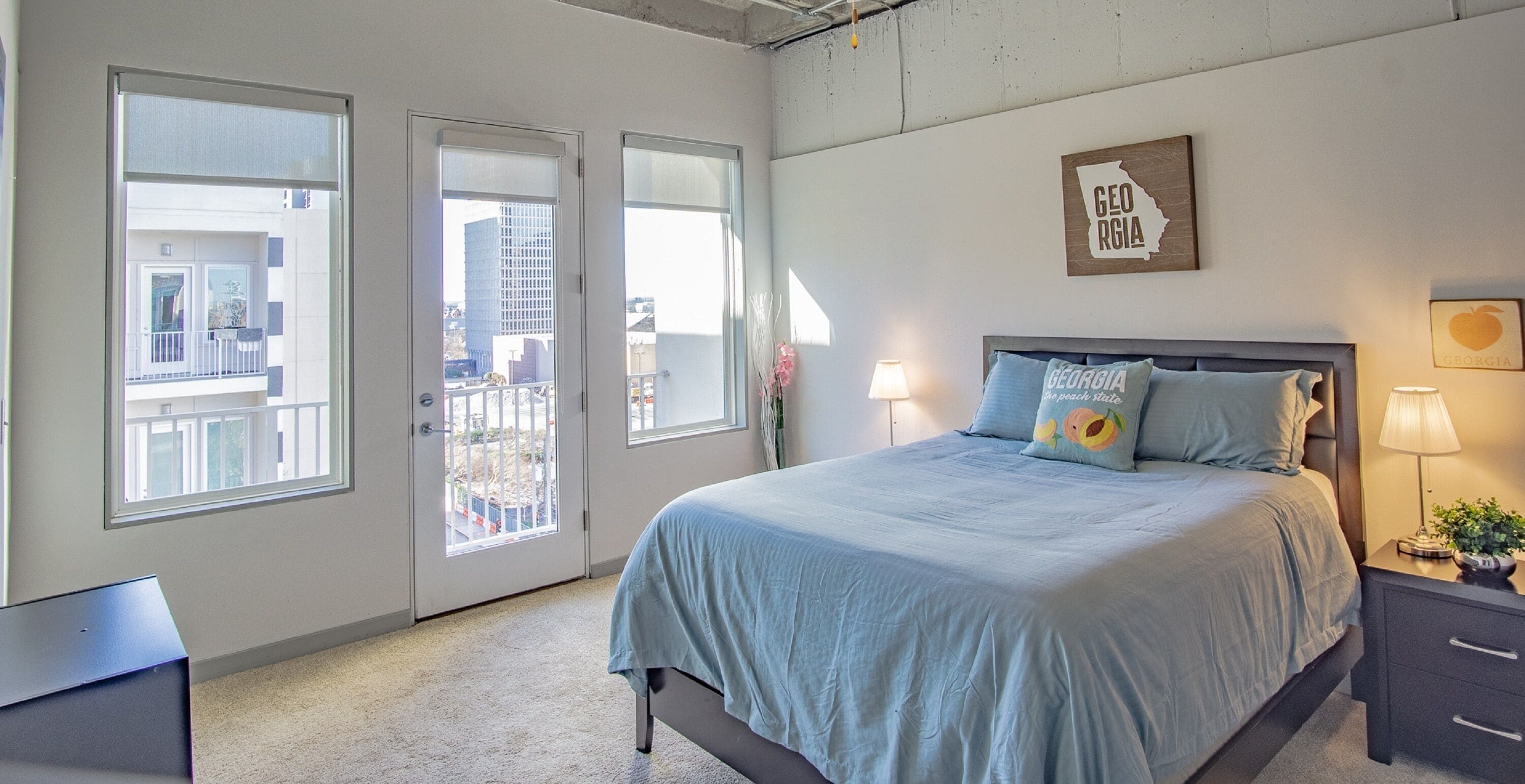 A bedroom with a bed, two bedside lamps, a nightstand, a window, and a door leading to a balcony.