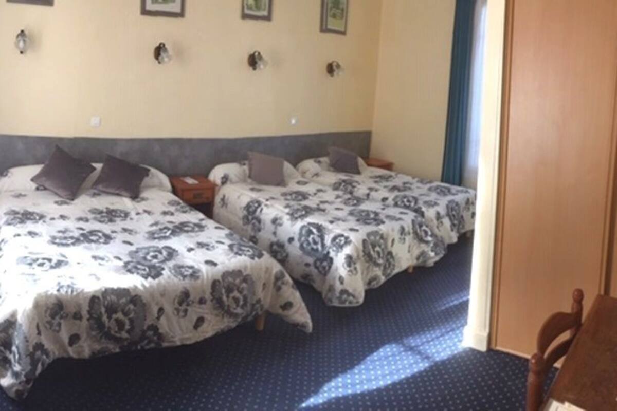 A room with two beds, each with patterned bedding and pillows, a wooden nightstand, and a small table.