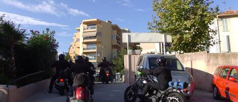 Un estacionamiento con motocicletas y un coche, rodeado de edificios y vegetación.