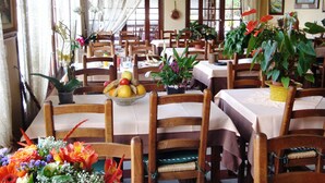 A dining area with wooden chairs and tables, decorated with potted plants and a fruit bowl. - Hôtel La Lubiane (Vence)
