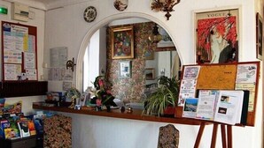 A reception area with a wooden counter, framed artwork, and a mirror reflecting the interior. - Hôtel La Lubiane (Vence)