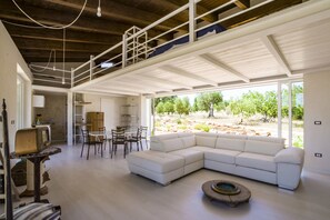 Un vaste espace de vie comprenant un canapé d’angle blanc, une table à manger avec des chaises, et un coin cuisine à l’arrière-plan.
