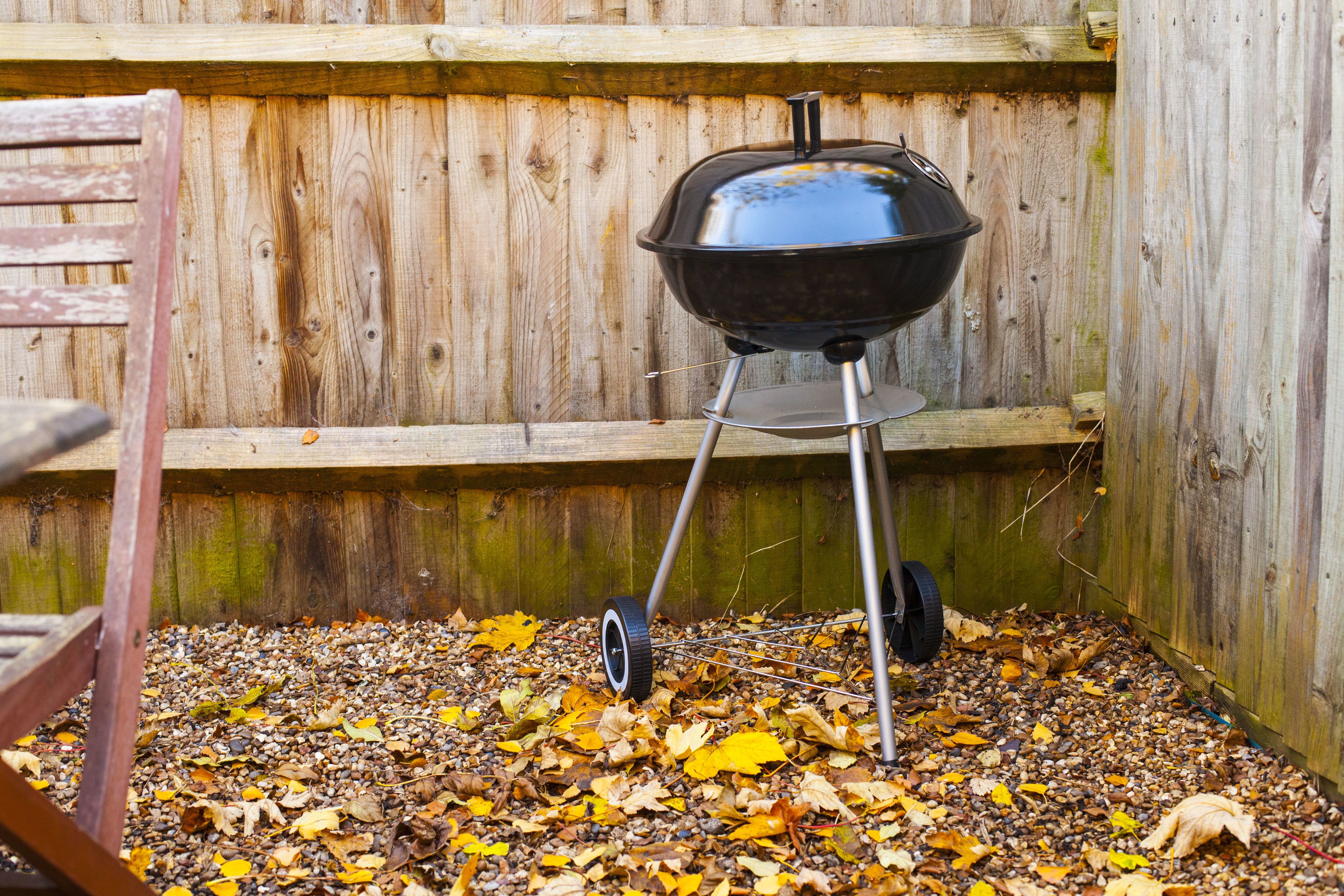 Una parrilla para barbacoa en un recinto de madera con una silla cerca.