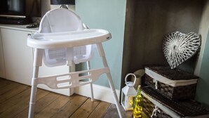 A white baby high chair in a room with a wooden floor, a television, a lamp, and decorative items on shelves. - Stunning Central Richmond with garden (Richmond)