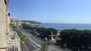 Un paisaje urbano costero con vista despejada al mar, una calle bordeada de coches aparcados y una estatua en primer plano.