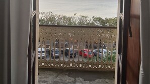 Un umbral abierto que da a un balcón con vista al mar y coches estacionados.