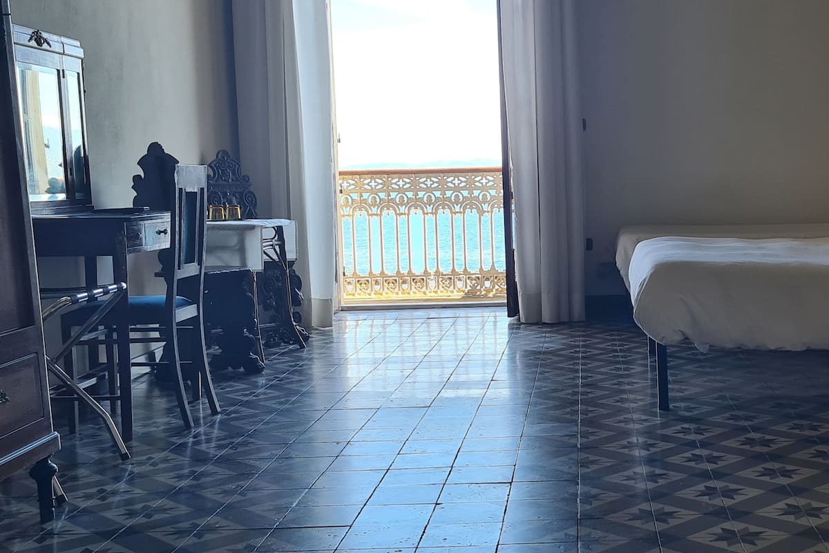 A room with a bed, a desk, and a chair. There is a balcony with a railing.