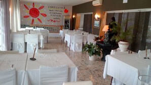 A restaurant with multiple tables set for dining, white tablecloths, and chairs with white covers. - Hostal Lleida (Calafell)
