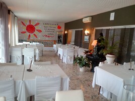 A restaurant with multiple tables set for dining, white tablecloths, and chairs with white covers.