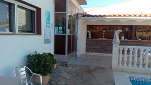 A patio area with a pool, a bar with a brick counter, a statue, and a seating area with a chair and a potted plant. - Hostal Lleida (Calafell)