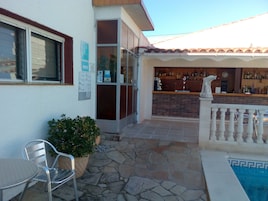 Un espace patio avec une piscine, un bar doté d’un comptoir en briques, une statue et un coin salon comprenant une chaise et une plante en pot.