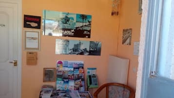 A room with a wooden door, a table with magazines and a phone, and a chair.