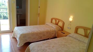 Une chambre avec deux lits, une porte donnant sur un balcon et une table de chevet avec une télécommande.