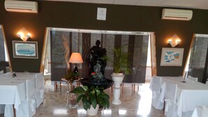 A restaurant with multiple tables covered in white tablecloths, a central decorative fountain, and potted plants. - Hostal Lleida (Calafell)