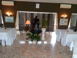 Un restaurant avec de nombreuses tables recouvertes de nappes blanches, une fontaine décorative au centre et des plantes en pot.