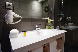 A modern bathroom with a white sink, a hairdryer, a mirror, and a shower. - Hotel Salomé (Calafell)