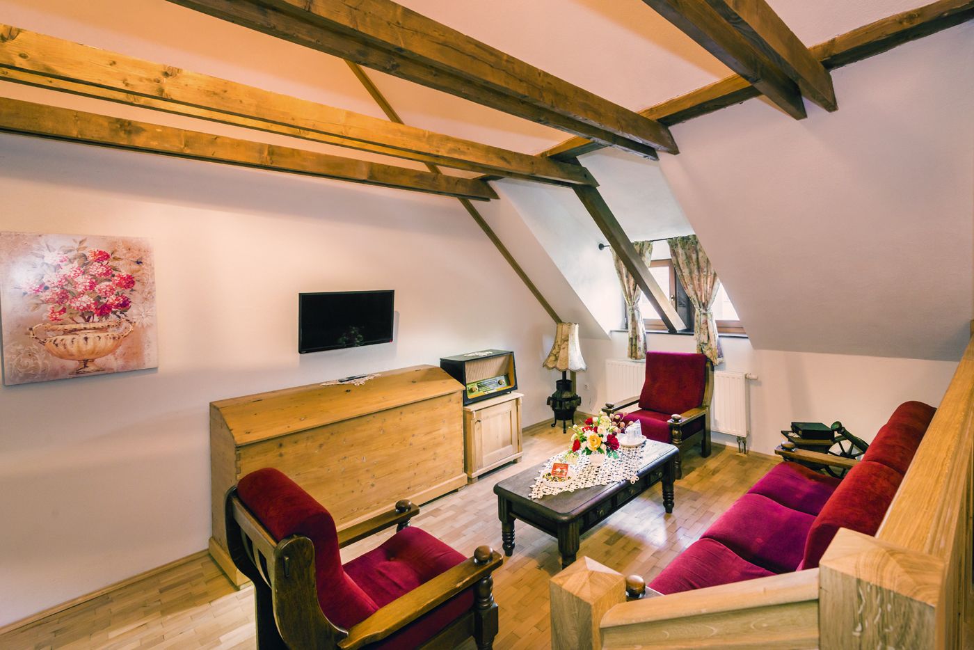 Um quarto estilo loft acolhedor, com vigas de madeira aparente, um banco de madeira, um sofá vermelho e uma pequena mesa com flores.