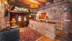 Un interior rústico con vigas de madera, pared de piedra, mostrador de recepción y una alfombra estampada.